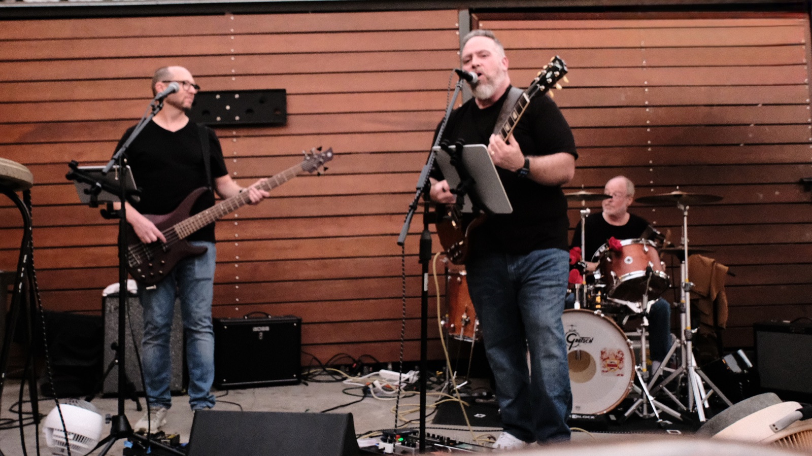 BGM playing on an outdoor stage — bass, guitar and vocals, and drums