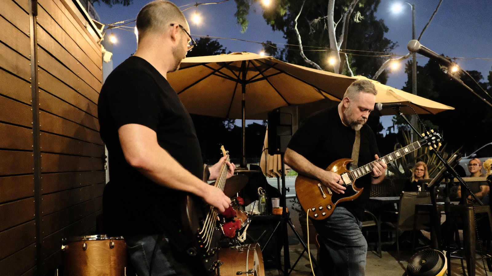Bass and guitar under string lights and patio umbrellas at dusk
